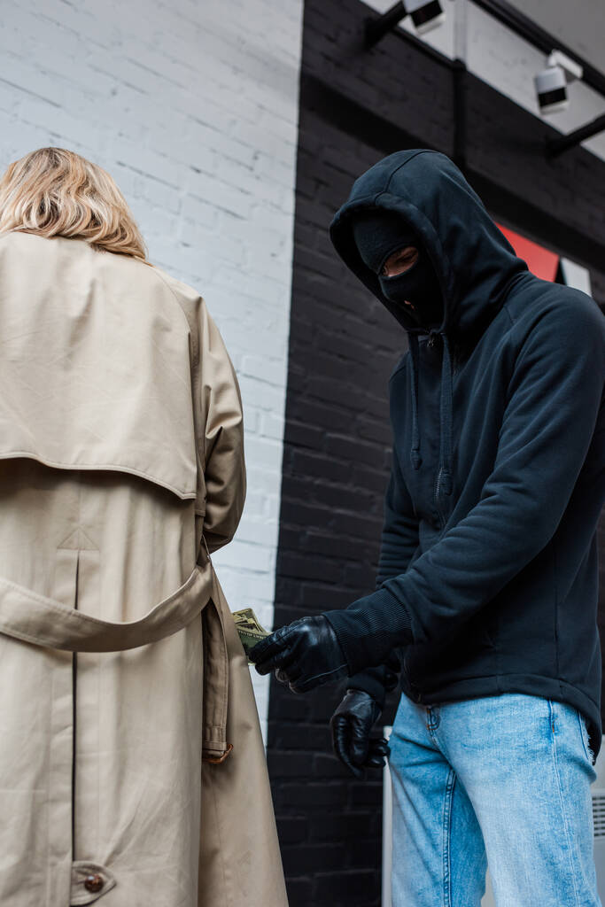 Kar maskeli soyguncunun düşük açılı görüntüsü kadının yanında para tutuyor.  - Fotoğraf, Görsel