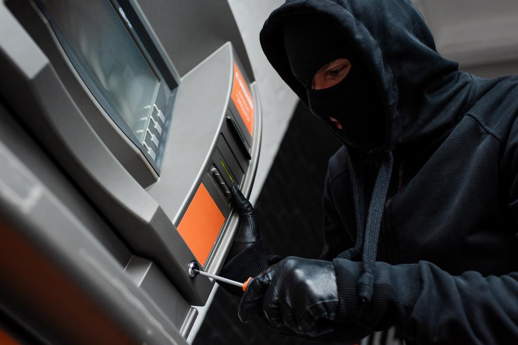 Low angle view of thief in balaclava using screwdriver while breaking atm  - Photo, Image
