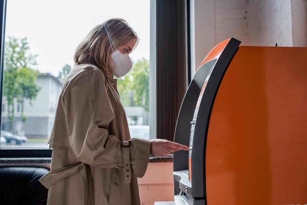 Seitenansicht einer Frau in medizinischer Maske mit Geldautomat  - Foto, Bild