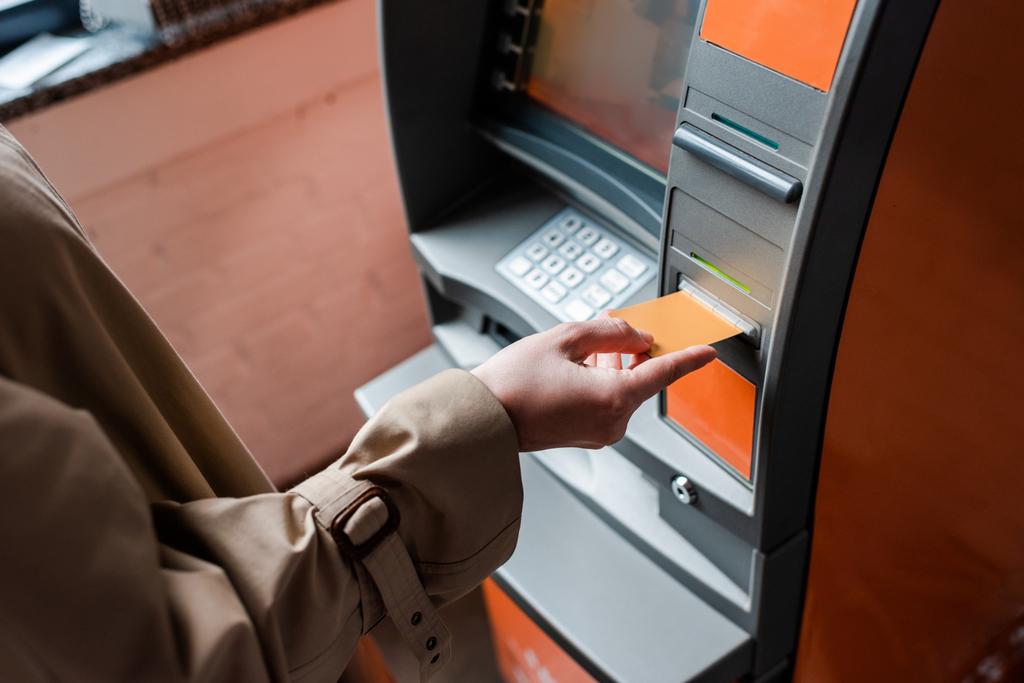 Ausgeschnittene Ansicht einer Frau, die Kreditkarte hält, während sie Geldautomaten benutzt  - Foto, Bild