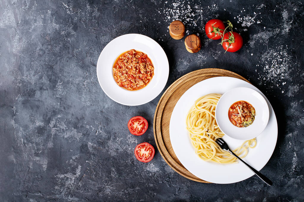 Spaghetti cotti bolognese serviti con pepe nero e saslt in piatto di ceramica bianca su fondo scuro. Vista dall'alto, posizione piatta. Copia spazio
 - Foto, immagini
