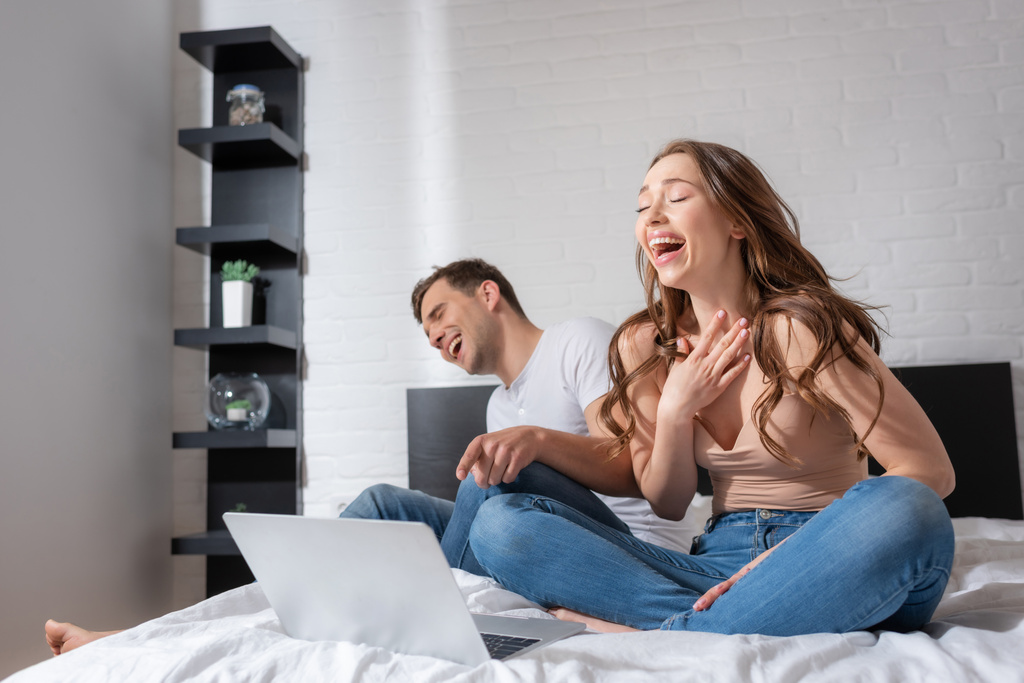 szelektív fókusz vidám nő és férfi nevet, miközben néz komédia film laptop a hálószobában  - Fotó, kép