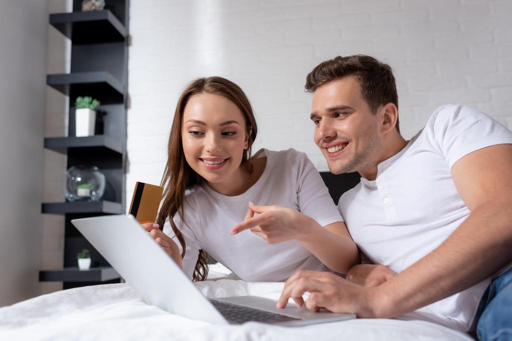 menina feliz apontando com o dedo para laptop e segurando cartão de crédito perto namorado
  - Foto, Imagem