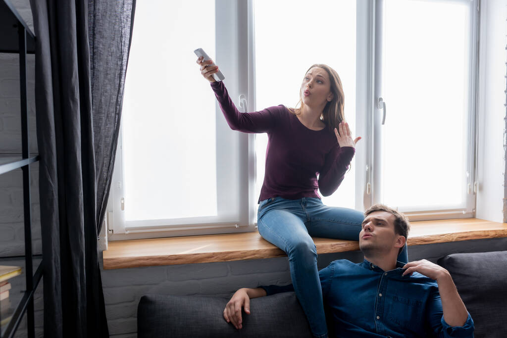 hombre disgustado cerca de mujer atractiva sosteniendo mando a distancia desde el aire acondicionado mientras se siente caliente
  - Foto, imagen