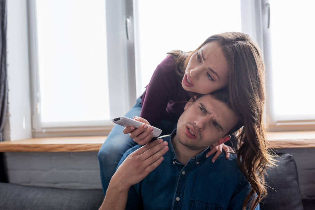 displeased man near woman holding remote controller from air conditioner while feeling hot  - Photo, Image