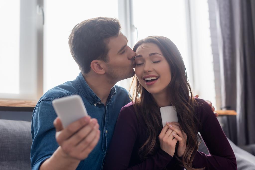 вибірковий фокус людини цілує щасливу дівчину і тримає смартфон
  - Фото, зображення