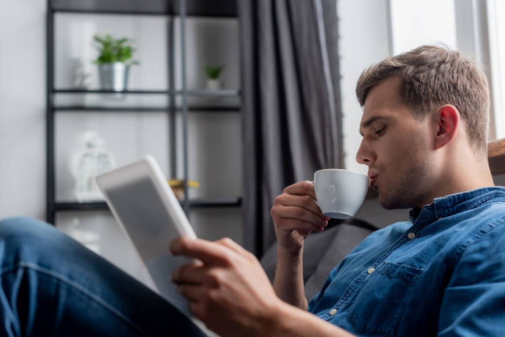 szelektív fókusz jóképű férfi holding csésze és digitális tabletta - Fotó, kép