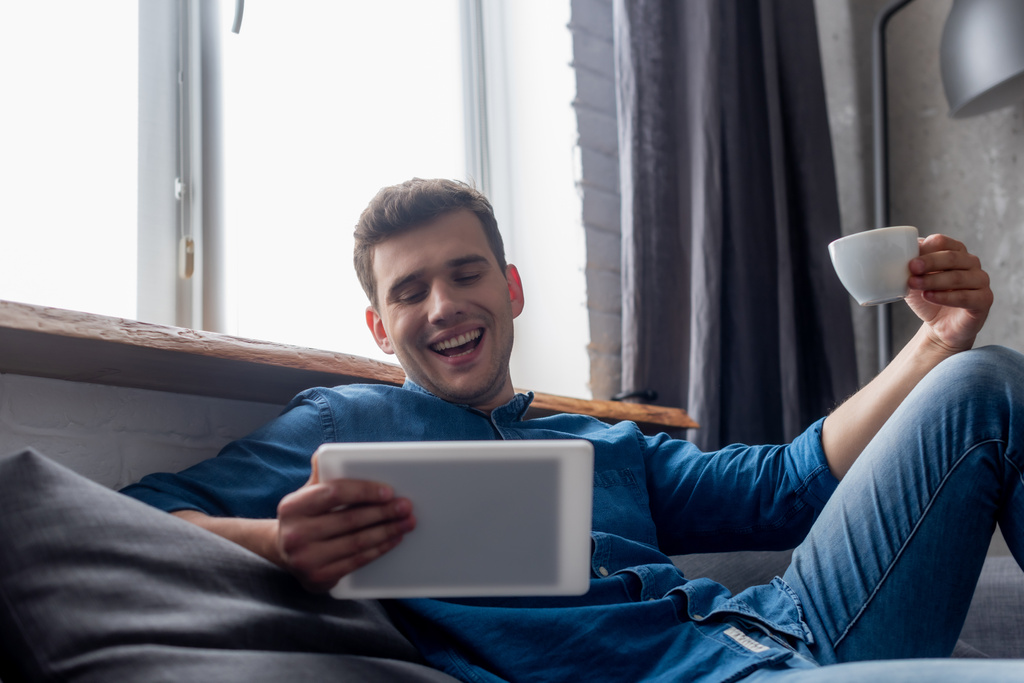 vrolijke man met een kopje koffie en kijken naar digitale tablet - Foto, afbeelding