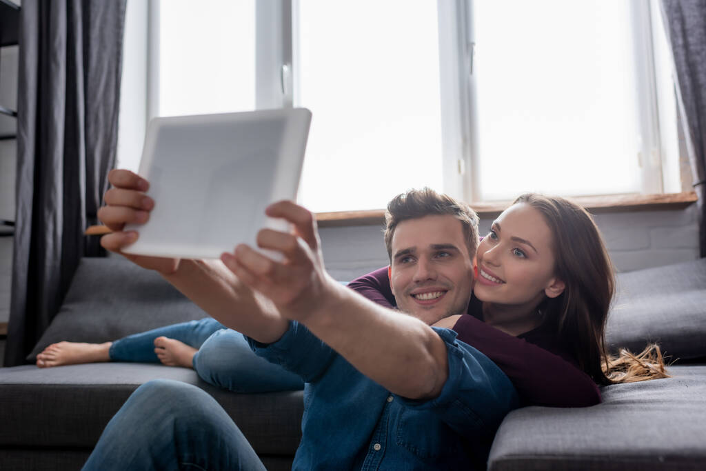 επιλεκτική εστίαση του χαρούμενος άνθρωπος λαμβάνοντας selfie με το κορίτσι, ενώ κρατώντας ψηφιακή ταμπλέτα  - Φωτογραφία, εικόνα
