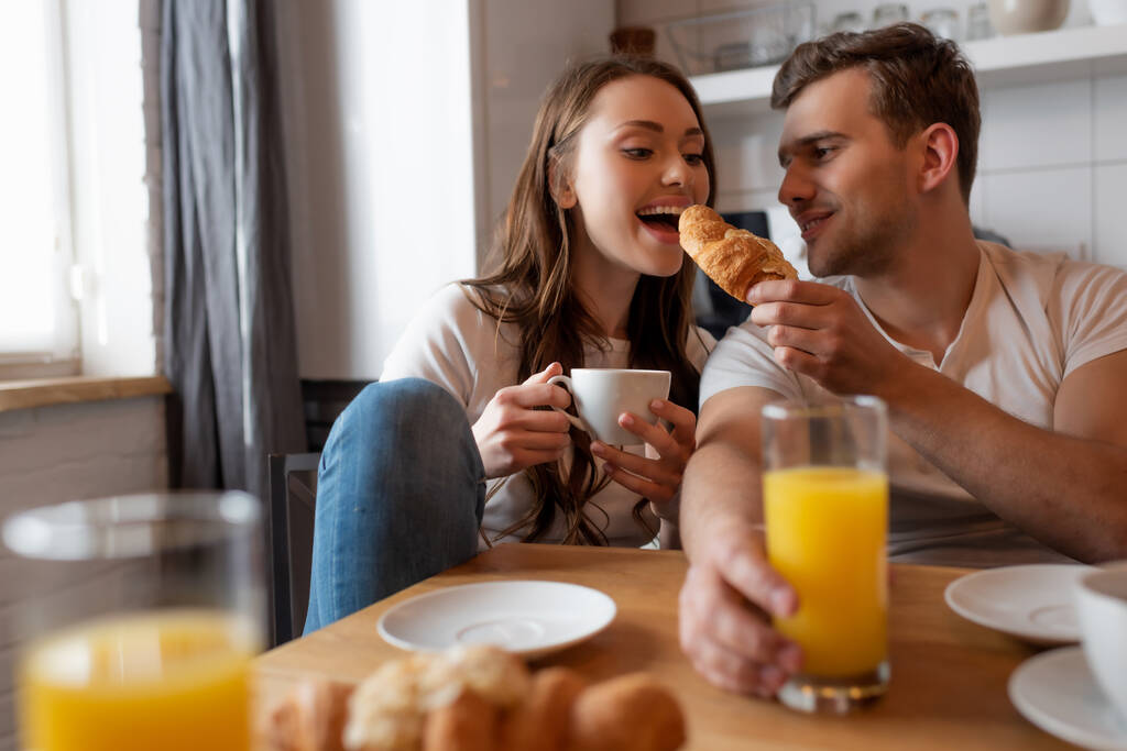 selektywne skupienie szczęśliwy człowiek karmienie wesoły dziewczyna z smaczne croissant  - Zdjęcie, obraz