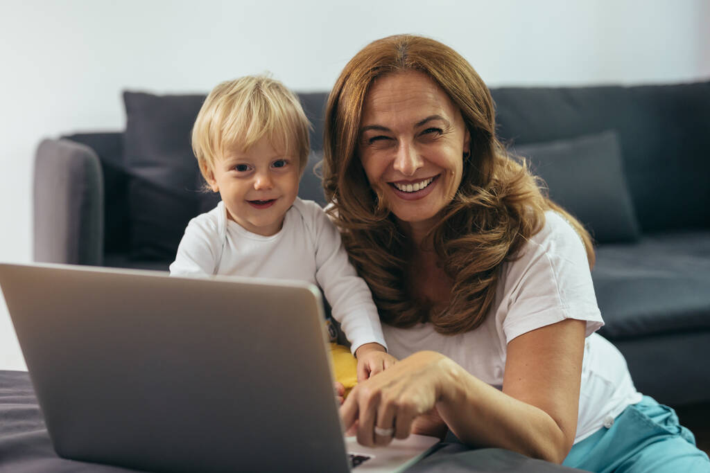 зріла жінка з онуком використовує ноутбук у себе вдома
 - Фото, зображення