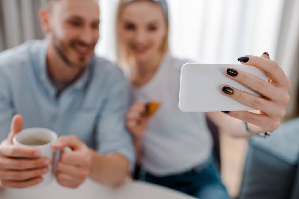 enfoque selectivo de la mujer feliz sosteniendo el teléfono inteligente y tomar selfie con el novio
  - Foto, Imagen