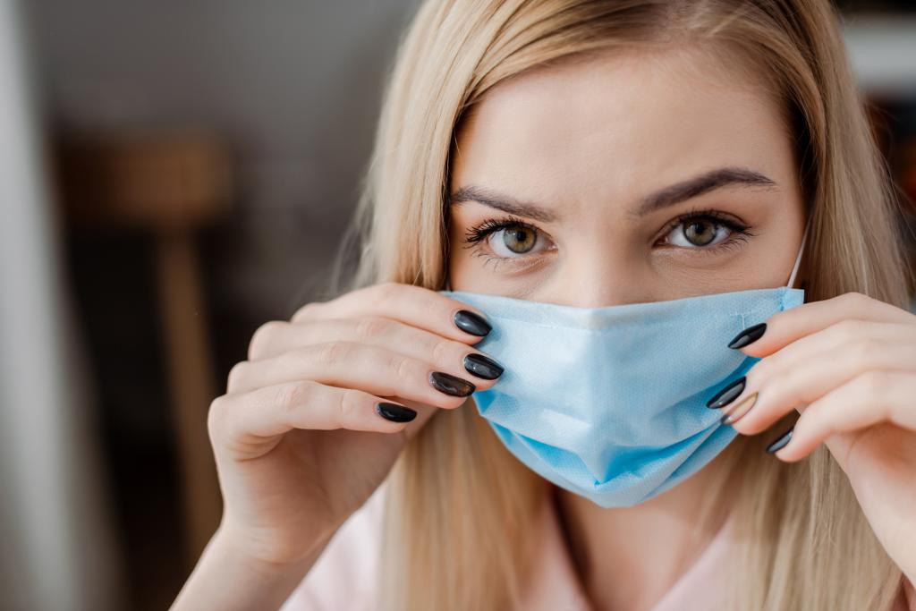 young woman looking at camera while touching medical mask  - Photo, Image