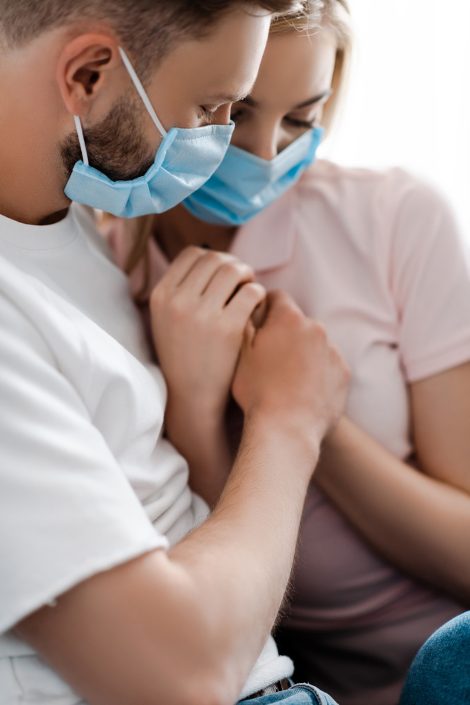 επιλεκτική εστίαση του ζεύγους σε ιατρικές μάσκες κρατώντας τα χέρια - Φωτογραφία, εικόνα