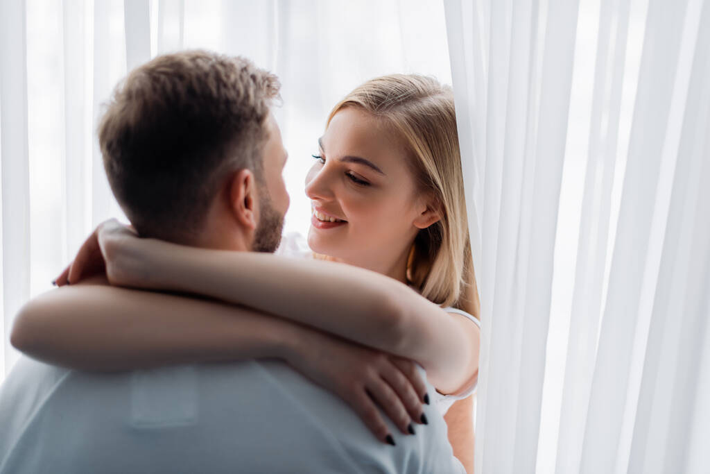 selective focus of smiling woman embracing and looking at boyfriend - Photo, Image