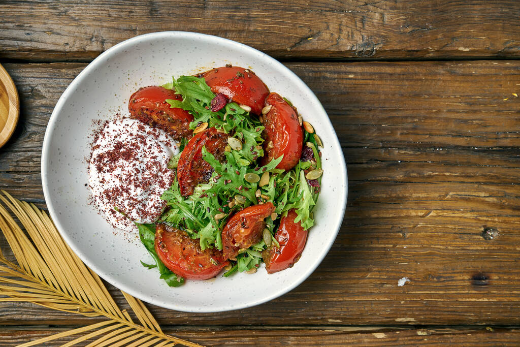 Insalata vegetariana con pomodori al forno, yogurt greco e rucola in una ciotola su uno sfondo di legno
 - Foto, immagini