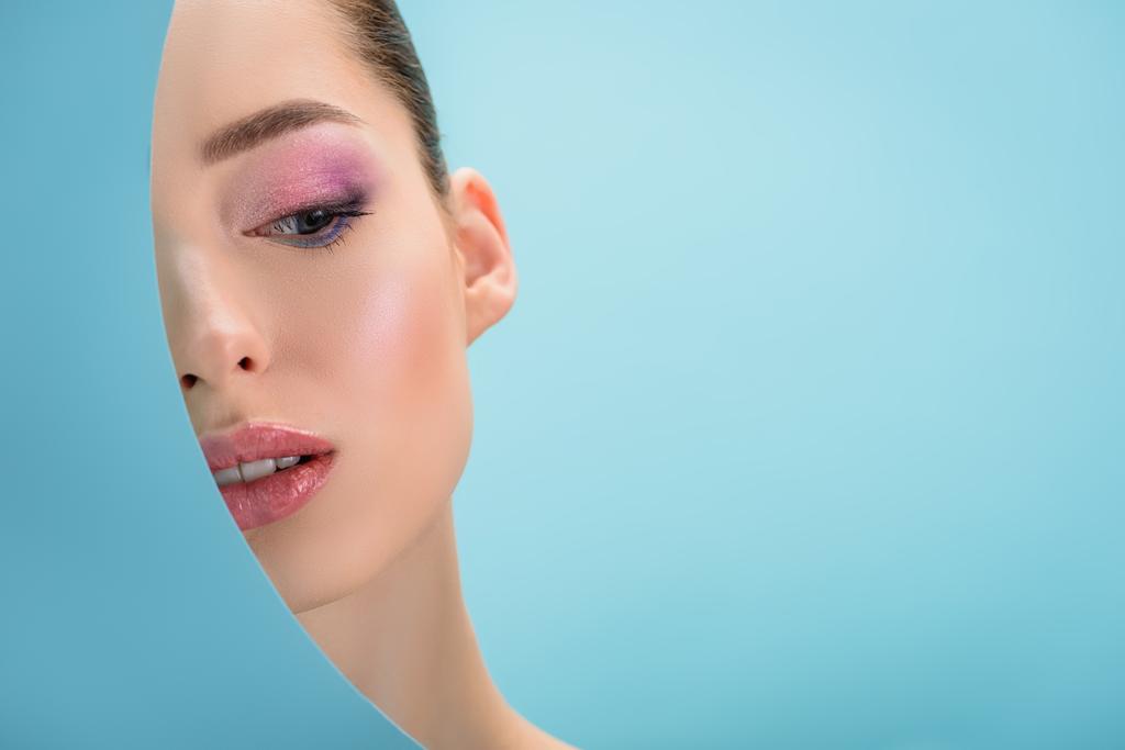 retrato de mujer hermosa con labios brillantes, sombra de ojos rosa detrás de agujero redondo de papel aislado en azul
 - Foto, Imagen