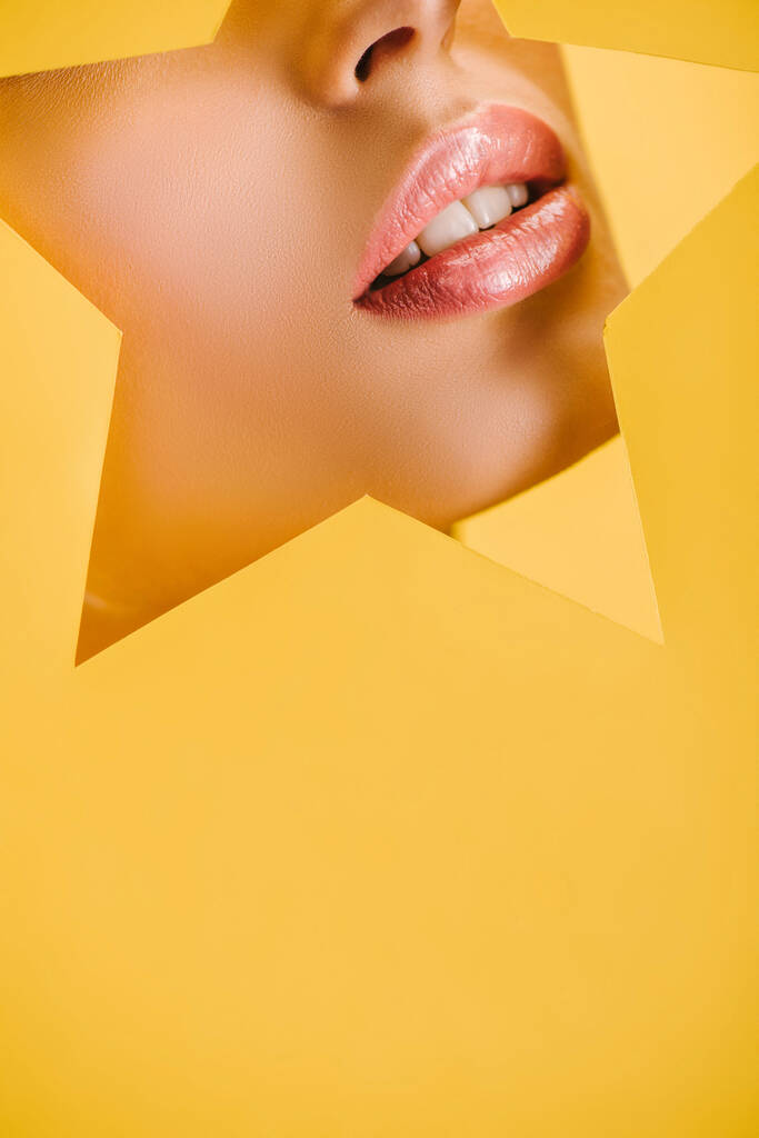 przycięty widok pięknej kobiety z błyszczącymi ustami w papierowym kształcie gwiazdy otwór izolowany na żółto - Zdjęcie, obraz