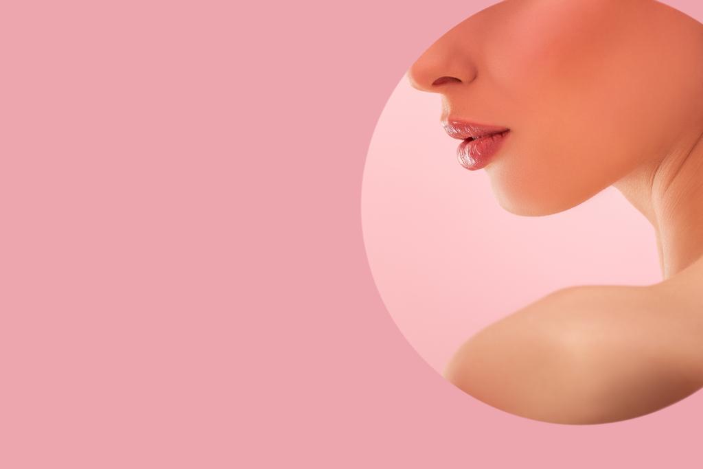 abgeschnittene Ansicht der schönen nackten Frau mit glänzenden Lippen in Papier runde Loch isoliert auf rosa - Foto, Bild