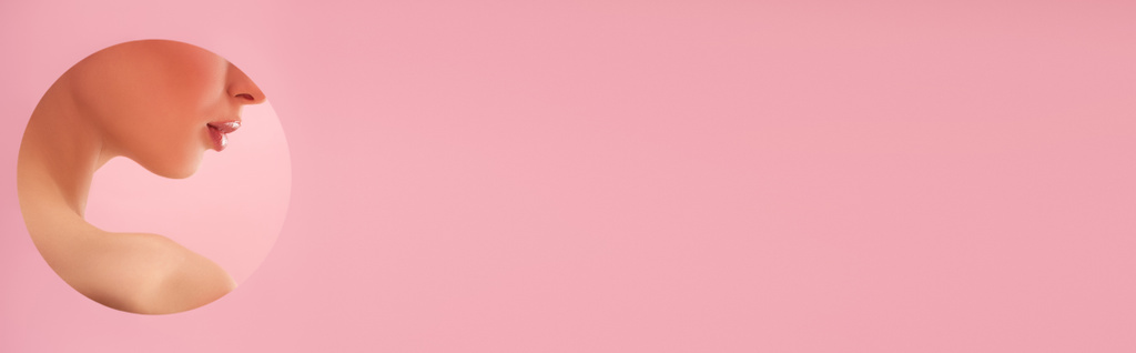 oříznutý pohled na krásnou nahou ženu s lesklými rty v papírové kulaté díře izolované na růžové, panoramatické záběry - Fotografie, Obrázek