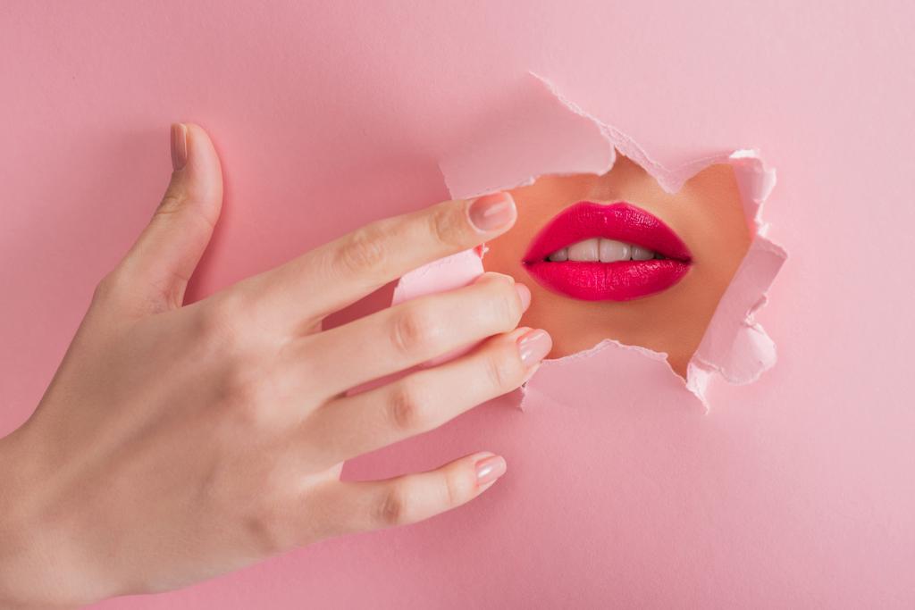 καλλιεργημένη άποψη της όμορφης γυναίκας με βυσσινί χείλη και λευκά δόντια σε χαρτί σχισμένο τρύπα απομονώνονται σε ροζ - Φωτογραφία, εικόνα