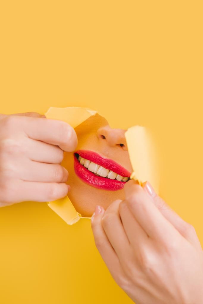 καλλιεργημένη άποψη της όμορφης γυναίκας με βυσσινί χείλη χαμογελώντας σε κίτρινο χαρτί σχισμένο τρύπα - Φωτογραφία, εικόνα