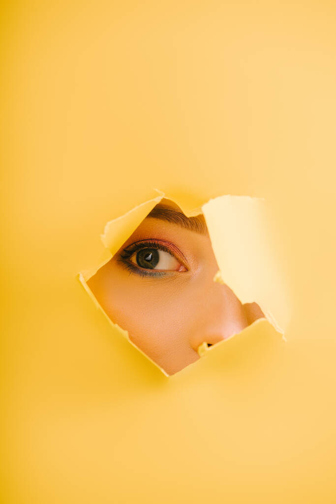 kivágott kilátás gyönyörű nő néz keresztül sárga papír szakadt lyuk - Fotó, kép