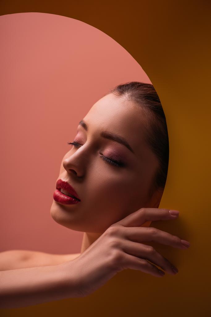 nackte schöne Frau mit purpurroten Lippen und geschlossenen Augen in Papierkreisloch im Dunkeln - Foto, Bild