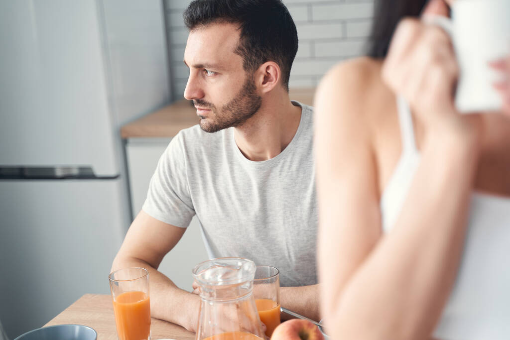 Nieszczęśliwy zmęczony mężczyzna jedzący śniadanie w domu z żoną - Zdjęcie, obraz