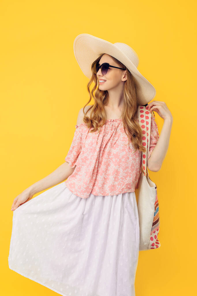 Szczęśliwa młoda atrakcyjna kobieta w letniej czapce i okularach przeciwsłonecznych, na odizolowanym żółtym tle - Zdjęcie, obraz