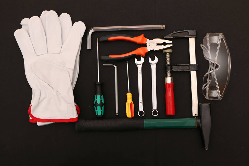 Un ensemble de nouveaux outils à main, masque, lunettes et gants sur fond noir. Un ensemble de nouveaux outils à main et d'équipements de protection pour un travail en toute sécurité sur un fond noir
. - Photo, image