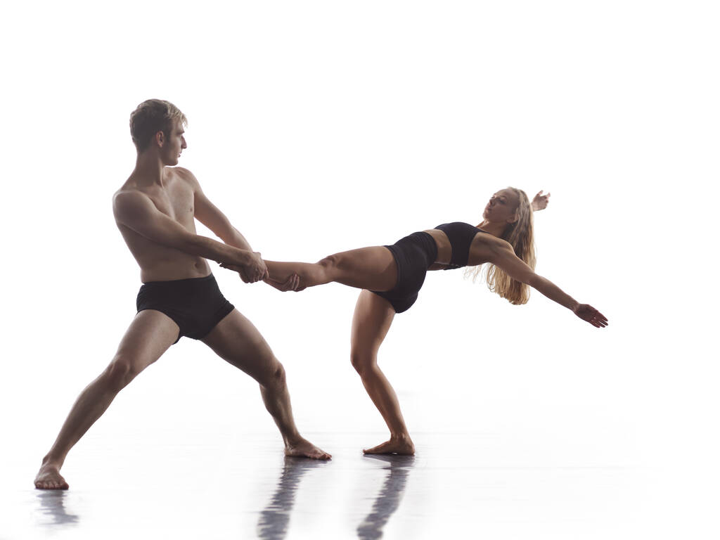 ブラックタイツの若いアスレチックダンスパートナーのカップルがアクロバティックな要素を作る現代的なスタイルのバレエを上演白い背景の前で芸術パフォーマンスのスポーティバレエダンサーのカップル - 写真・画像