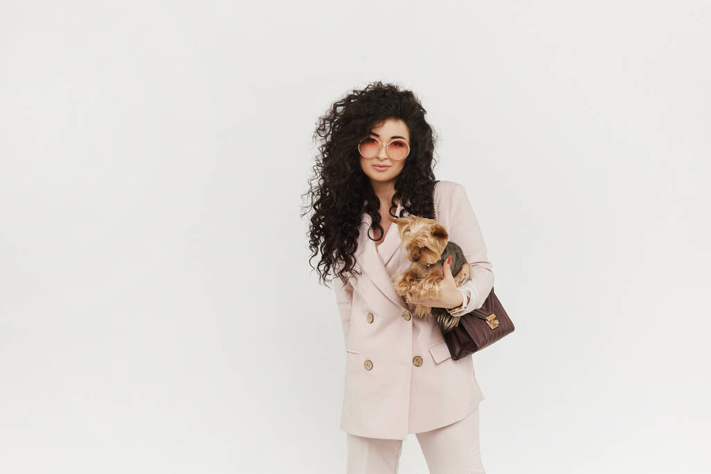 Stílusos lány hivatalos ruhában tartja aranyos kis kutya a kezében, és pózol fehér háttér, elszigetelt. Városi divat. - Fotó, kép