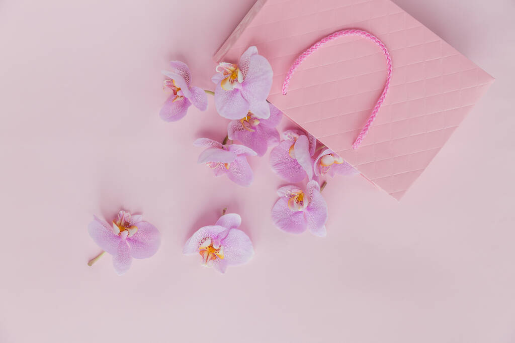 Розовый подарочный пакет и летающие цветы орхидеи на светло-розовом фоне. Открытка с нежными цветами. Праздник, Женский день, День матери
. - Фото, изображение