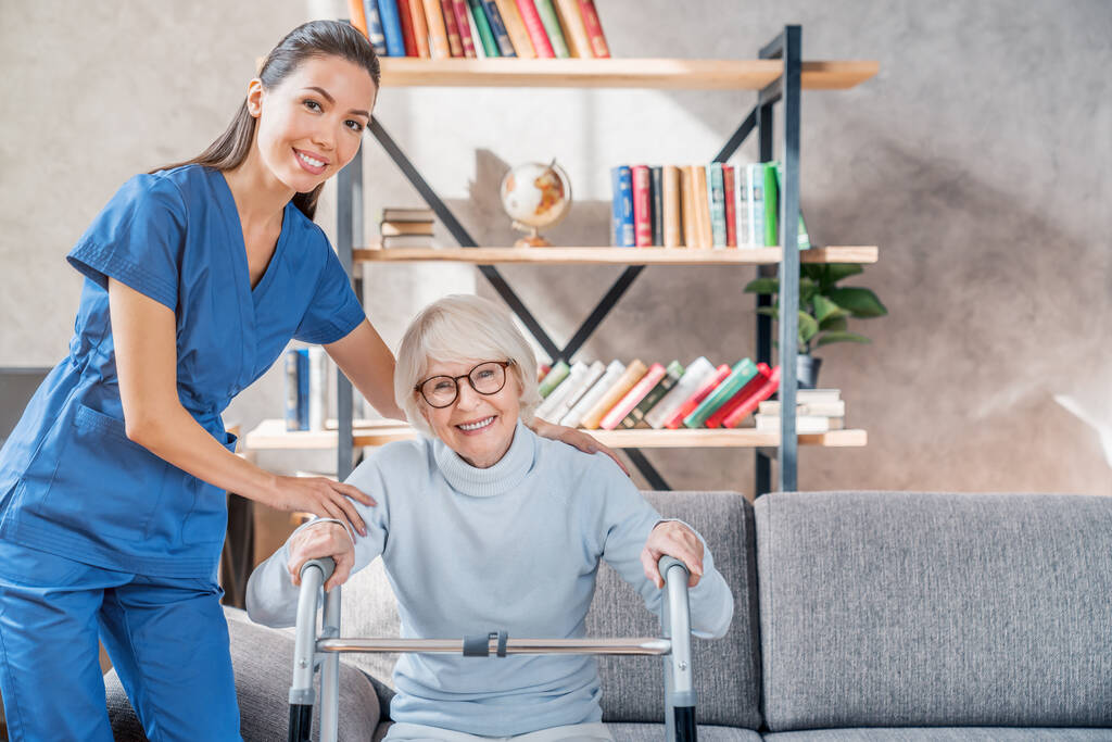 Жіноча азіатська медсестра допомагає старшій жінці вставати з ходунками вдома
 - Фото, зображення