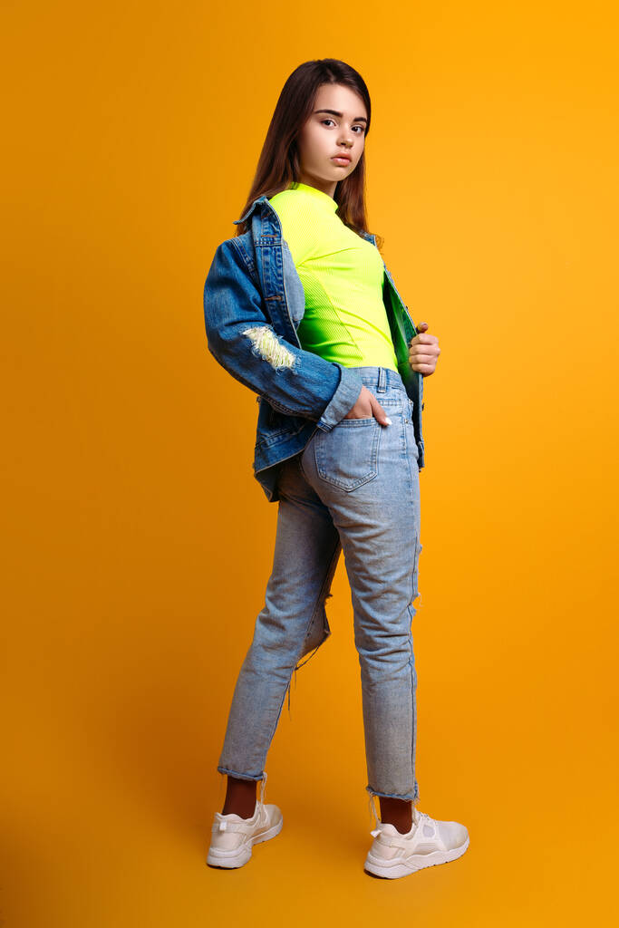jong tiener meisje gekleed in jeans en een jas in de studio op een gele achtergrond - Foto, afbeelding