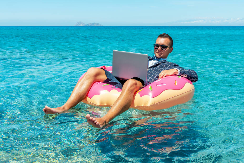 Homme d'affaires utilisant un ordinateur portable sur un beignet gonflable dans la mer. Concept vacances d'été. - Photo, image