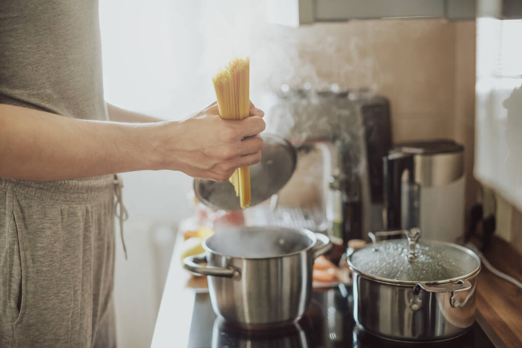 Mies kokkaa pastaspagettia kotona keittiössä. Kotiruokaa tai italialainen ruoanlaitto käsite.  - Valokuva, kuva