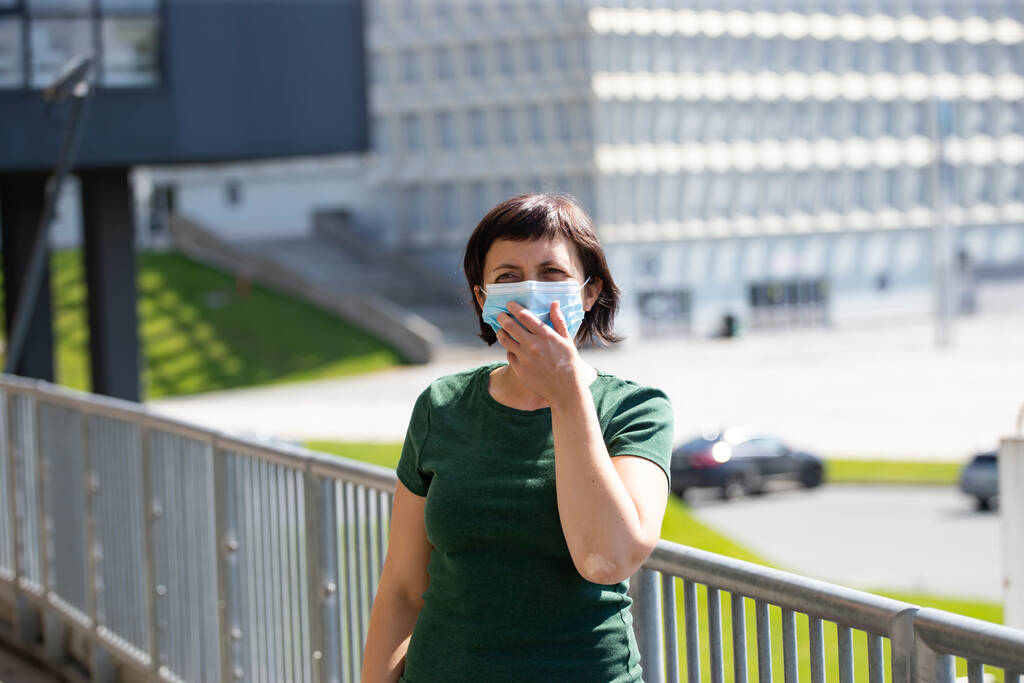 COVID-19パンデミックコロナウイルス。近代的な建物の前の女性は、疾患ウイルスSARSのCoV-2の普及のための顔マスク保護を身に着けています.女性の顔に保護マスクのコロナウイルス病に対する. - 写真・画像