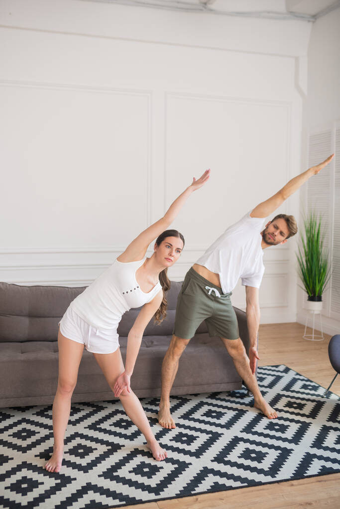Jovem casal em camisetas brancas tendo treino em casa e inclinação
 - Foto, Imagem