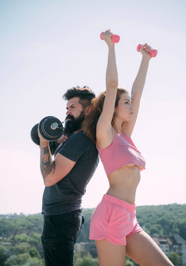 Beautiful brunette woman and bearded handsome man doing sport fitness activities at clear sky background. Attractive young couple do fitness exercises during their leisure time. - Photo, Image