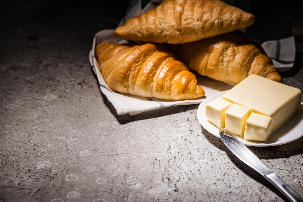 tuoreet croissantit pyyhkeellä lähellä voita ja veitsi betoninharmaalla pinnalla pimeässä - Valokuva, kuva