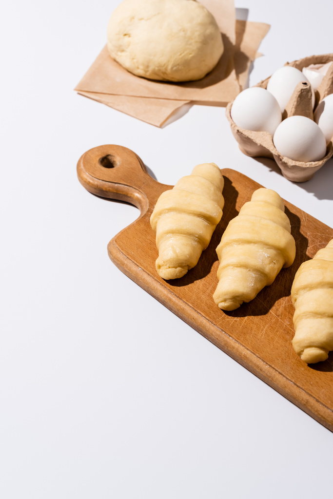 сирі круасани на дерев'яній обробній дошці біля яєць і тіста на білому тлі
 - Фото, зображення