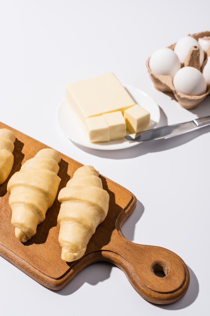 селективний фокус сирих круасанів на дерев'яній обробній дошці біля масла, яйця на білому тлі
 - Фото, зображення