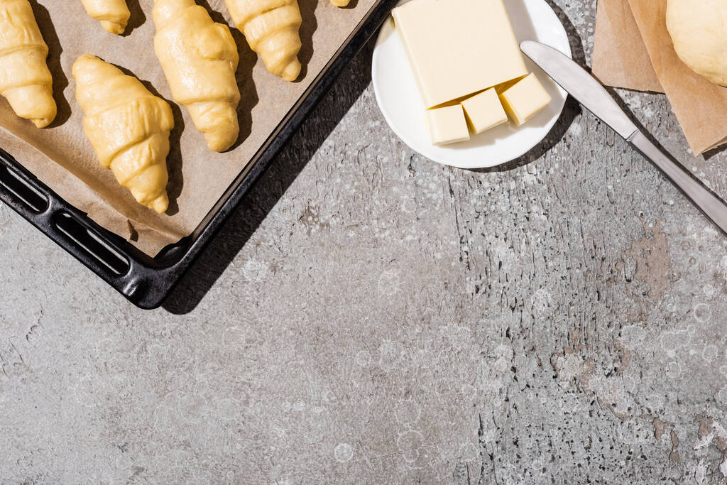 felülnézet főzés nélküli croissant sütő tálcán közel tészta és vaj beton szürke felületen - Fotó, kép