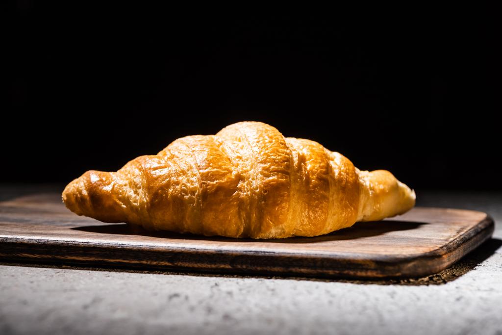 fresh baked croissant on wooden cutting board on concrete grey surface isolated on black - Photo, Image