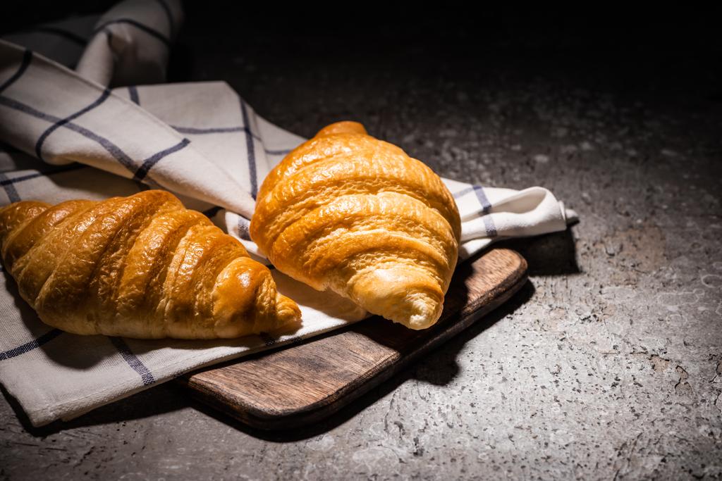 friss sült croissant törölközőn és fa vágódeszka betonszürke felületen sötétben - Fotó, kép