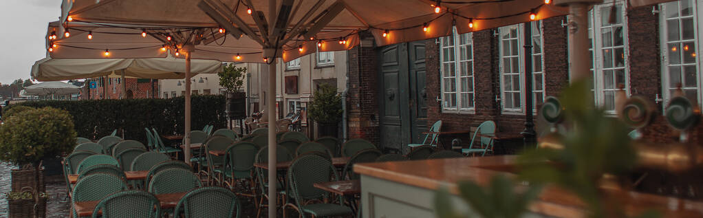 Coltivazione panoramica di illuminazione su ombrelloni di vicino tavoli e sedie di caffè all'aperto a Copenaghen, Danimarca  - Foto, immagini