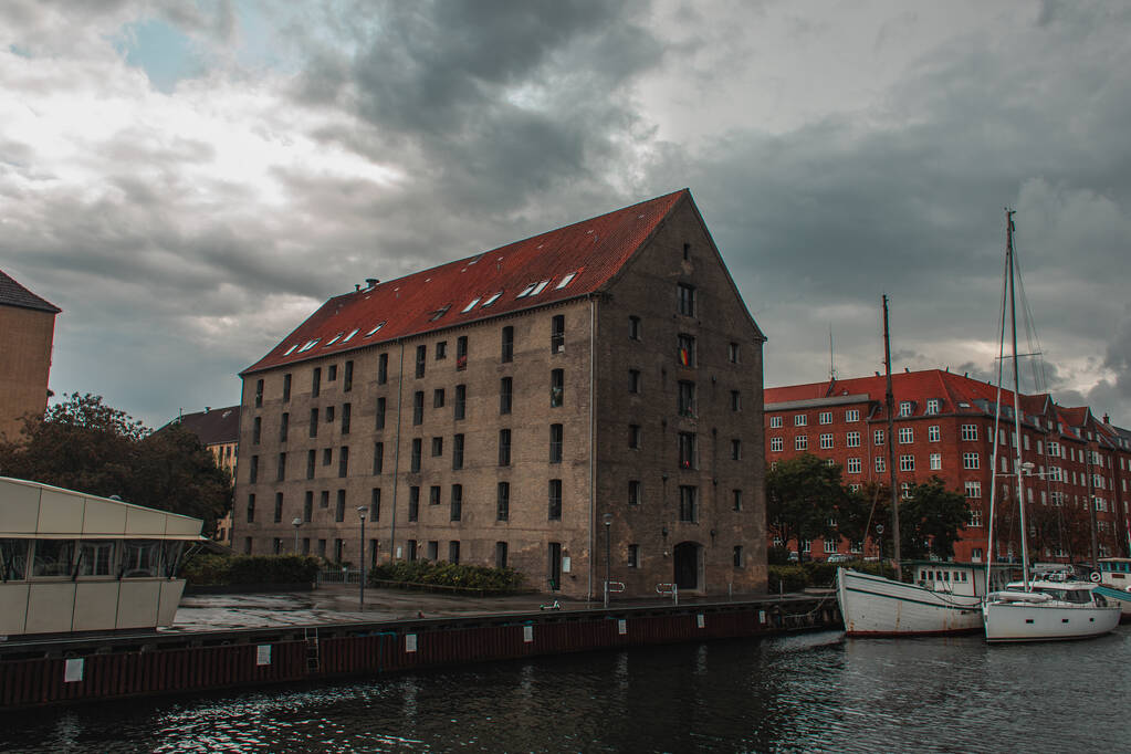 Buildings near harbor and boats on water with cloudy sky at background in Copenhagen, Denmark  - Photo, Image