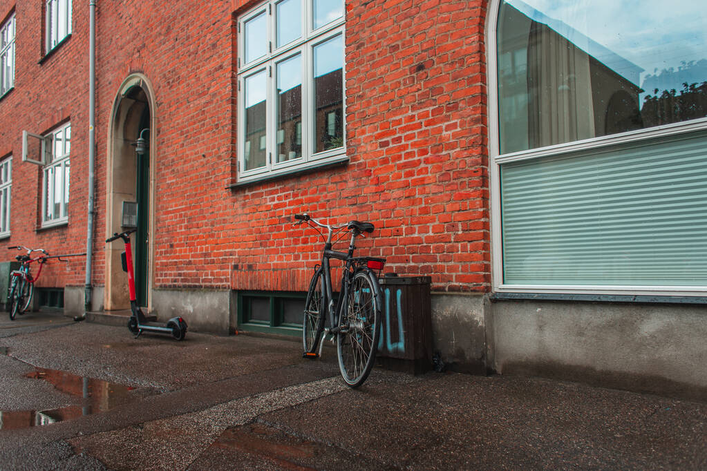 Rowery i skutery w pobliżu ceglanej fasady budynku przy ulicy miejskiej w Kopenhadze, Dania  - Zdjęcie, obraz